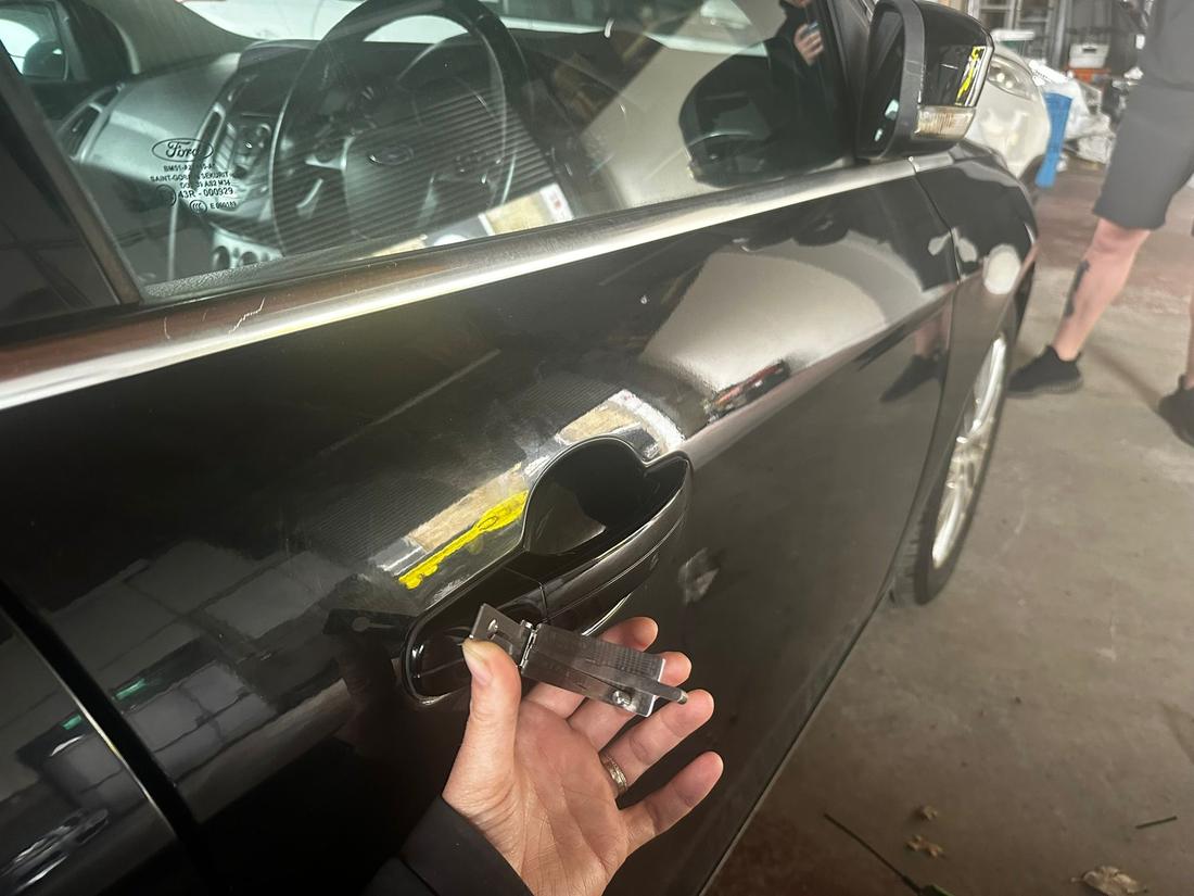 Auto locksmith programming a key at a black Ford in the workshop