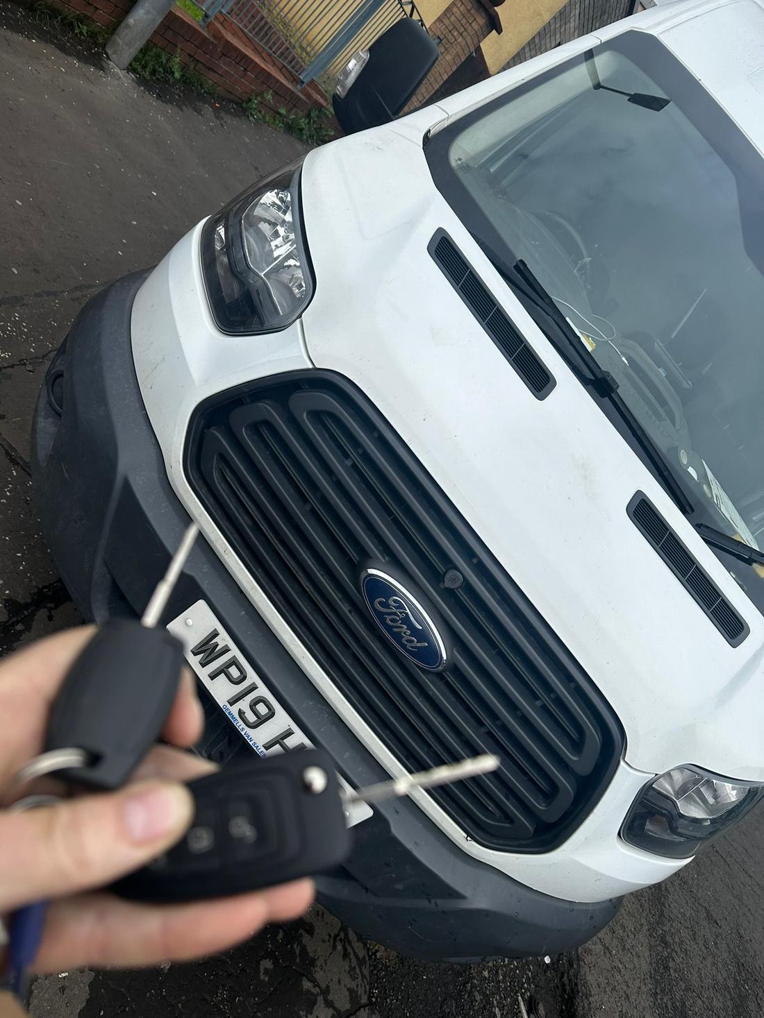 Newly cut and programmed Ford keys held in front of a Transit van