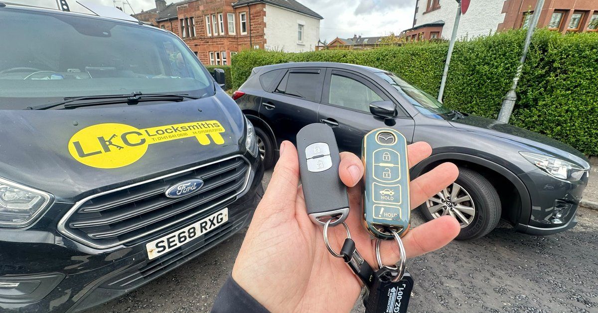 Two Mazda car keys held beside the branded LKC Locksmiths van after a car key job in Kilmarnock